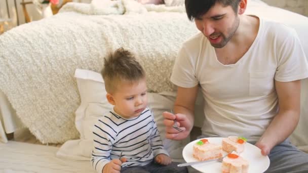 Schattig jongetje viert zijn verjaardag met jonge vader taart eten in slaapkamer — Stockvideo