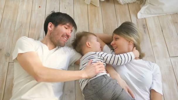 Vista superior del padre y la madre guapos jugar y abrazar a su hijo pequeño mientras está acostado en el suelo — Vídeo de stock