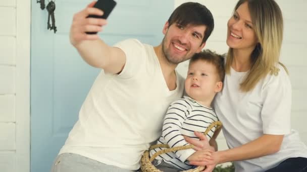 Батько щасливої сім'ї робить селфі з дружиною і маленьким сином перед їх рідними дверима — стокове відео