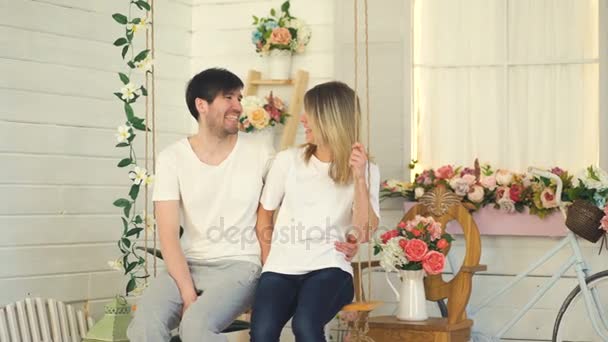 Счастливая любящая пара, сидящая на качелях и разговаривающая дома в саду — стоковое видео