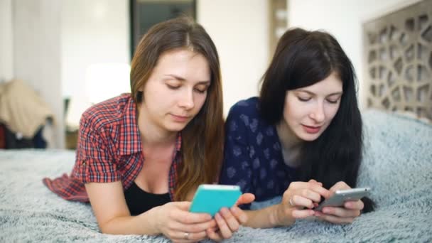 Dos amigas felices compartiendo redes sociales en un teléfono inteligente y hablando — Vídeos de Stock