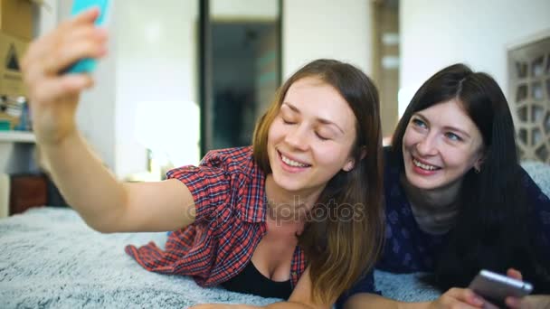 Счастливые веселые сестры делают селфи по утрам и веселятся на кровати в спальне дома — стоковое видео