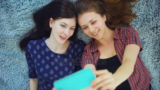 Top view of two pretty girls in pajamas making selfie portrait on bed in bedroom at home — Stock Video