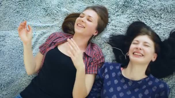 Κάτοψη του δύο όμορφα κορίτσια σε ακουστικά ακούγοντας μουσική, χορό και χαμογελώντας ενώ ξαπλωμένος στο κρεβάτι — Αρχείο Βίντεο