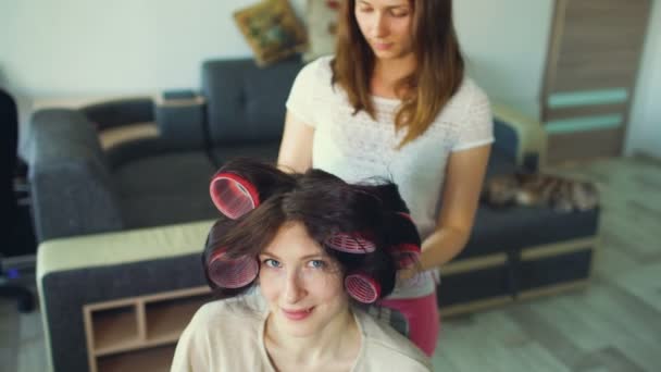 Engraçado mulher sorriso enquanto sua girlfrind fazer divertido curler penteado — Vídeo de Stock