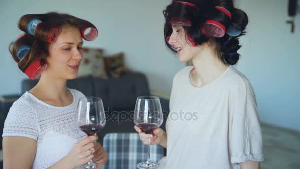 Dos amigas felices con rizador divertido peinado beber vino y hablar en casa — Vídeos de Stock