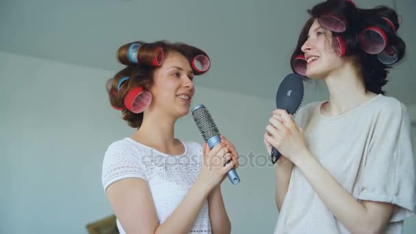 Zwei lustige Mädchen, die mit Kämmen singen, tanzen und haben Freude im heimischen Wohnzimmer — Stockvideo