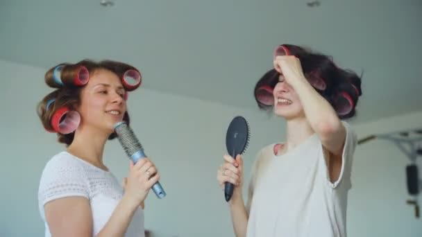 Twee grappige meisjes zingen met kammen dansen en hebben plezier in de huiskamer — Stockvideo