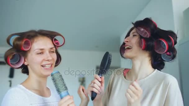 Dos chicas divertidas cantando con peines bailan y tienen alegría en la sala de estar en casa — Vídeos de Stock