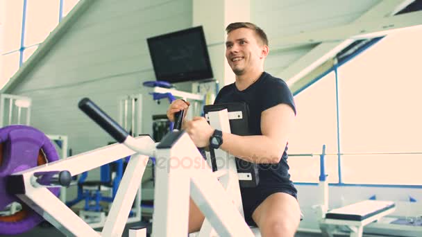 Bonito homem esportivo está se exercitando e sorrindo no clube de fitness e centro de fitness — Vídeo de Stock