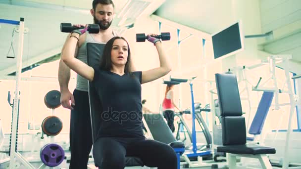 Trainer helps young strong brunette woman doing exercise in fitness club and gym center — Stock Video