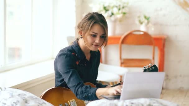 Ελκυστική νεαρή κοπέλα που μαθαίνουν να παίζουν κιθάρα ηλεκτρική με σημειωματάριο κάθονται στο κρεβάτι στο υπνοδωμάτιο στο σπίτι — Αρχείο Βίντεο
