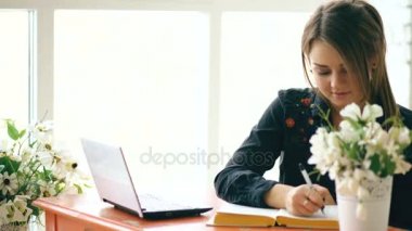Dizüstü bilgisayar ve yazma kitap kapalı kafede oturan genç güzel kadın öğrenci