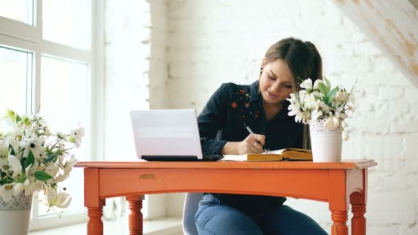 Student van de jonge mooie vrouw zitten met laptop en schrijven boek bij café binnen — Stockvideo