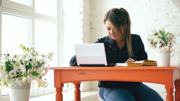 Молодая красивая студентка сидит с ноутбуком и пишет книгу в кафе в помещении — стоковое видео