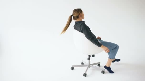 Happy young girl ride white modern office chair and have fun on white background — Stock Video