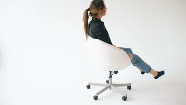 Happy young girl ride white modern office chair and have fun on white background — Stock Video