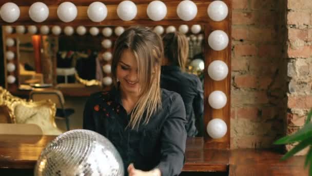 Movimento lento de bela jovem com bola de discoteca posando e sorrindo em estúdio dentro de casa — Vídeo de Stock