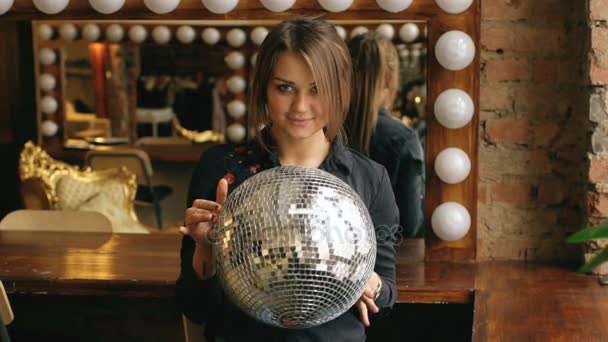Movimento lento de bela jovem com bola de discoteca posando e sorrindo em estúdio dentro de casa — Vídeo de Stock
