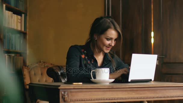 Медленное движение улыбающейся студентки, работающей на ноутбуке в университетской библиотеке в помещении — стоковое видео