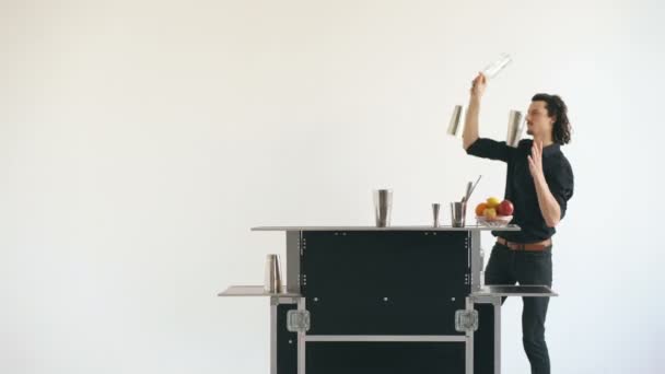 Professinal bartender man juggling bottles and shaking cocktail at mobile bar table on white background studio indoors — Stock Video