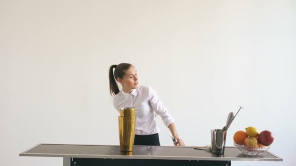 Professionele barman meisje jongleren flessen en schudden cocktail aan mobiele bar tafel op witte achtergrond — Stockvideo