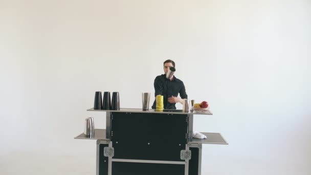 Άνθρωπος μπάρμαν professinal juggling μπουκάλια και τίναγμα κοκτέιλ στο μπαρ κινητό τραπέζι σε άσπρο φόντο — Αρχείο Βίντεο