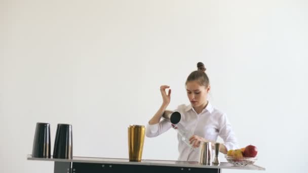 Professionele barman meisje jongleren flessen en schudden cocktail aan mobiele bar tafel op witte achtergrond studio binnenshuis — Stockvideo