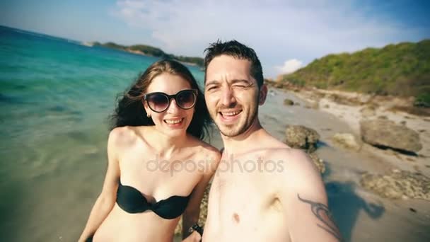 Молода щаслива пара розмовляє з друзями через інтернет, використовуючи смартфон на океанському пляжі — стокове відео