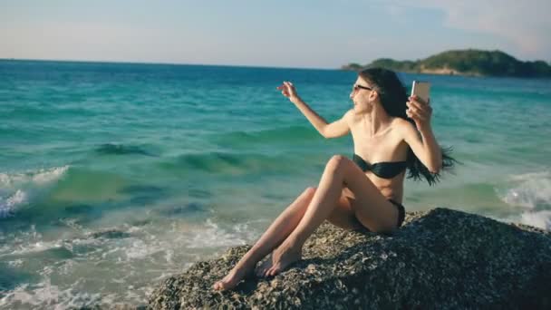 Mladá šťastná žena, chatování s přáteli prostřednictvím Internetu pomocí smartphone v ocean beach — Stock video