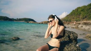 Deniz kenarında plajda kablosuz kulaklıklar müzik dinlerken mutlu güzel kadın