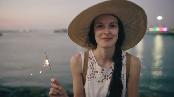 Vacker tonårsflicka i hatt med burn tomtebloss och leende på stranden vid solnedgången — Stockvideo