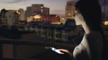 Genç kadın manifatura çatı katı terasında smartphone ayakta geceleri üzerinde gülümseyen closeup