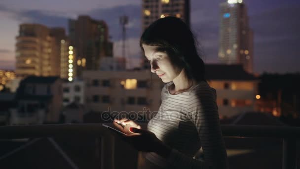若い女性夜屋上テラスでスマート フォンの立っている上にテキスト メッセージの笑みを浮かべてクローズアップコア — ストック動画