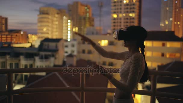Mujer joven en la terraza de la azotea con auriculares de realidad virtual y experiencia VR por la noche — Vídeos de Stock