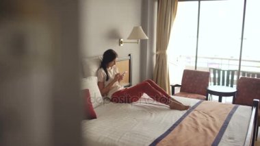 Sarışın kadın otel odasında yatakta yalan güzel ve akıllı telefon ve gülümseyen kullanın
