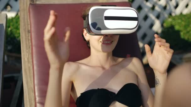Νεαρή γυναίκα ντυμένη με ένα ακουστικό γυαλιά εικονικής πραγματικότητας σε πισίνα ξενοδοχείου — Αρχείο Βίντεο