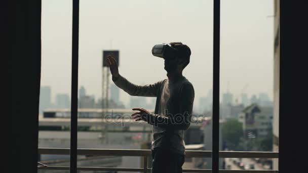 Silhouette eines jungen Mannes, der Film in vr Headset anschaut und Virtual-Reality-Erfahrung auf dem Hotelzimmerbalkon hat — Stockvideo