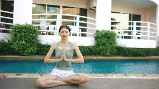 Mujer tranquila haciendo yoga cerca de la piscina en el hotel en un día soleado — Vídeo de stock