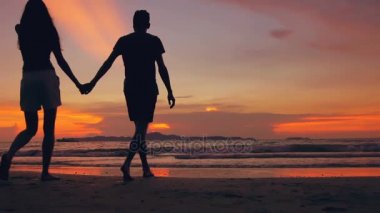 Mutlu sevgi dolu çift silüeti ağır çekim karşılamak ve kumsala günbatımı üzerinde okyanus kıyısında gidelim.