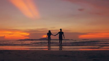 Mutlu sevgi dolu çift silüeti yavaş hareket okyanus kıyısında on sunset beach adlı yürüyüş