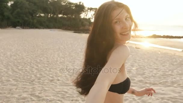 Slow motion av Följ mig skott av ung sexig tjej i bikini kör och håller man i handen på stranden i solnedgången — Stockvideo