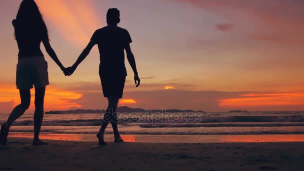 Silhouette au ralenti d'un couple heureux et aimant se rencontrent et vont à la plage au coucher du soleil au bord de l'océan — Video