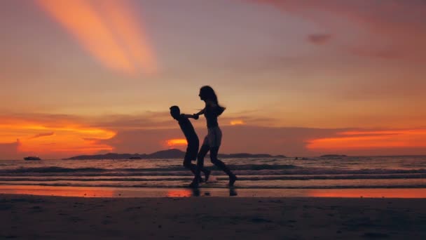 Медленно движущийся силуэт счастливой влюбленной пары встречает и играет на пляже на закате океана — стоковое видео