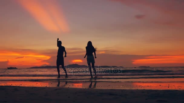 A silhueta de câmera lenta do casal amoroso feliz se encontra e brinca na praia ao pôr do sol na costa oceânica — Vídeo de Stock