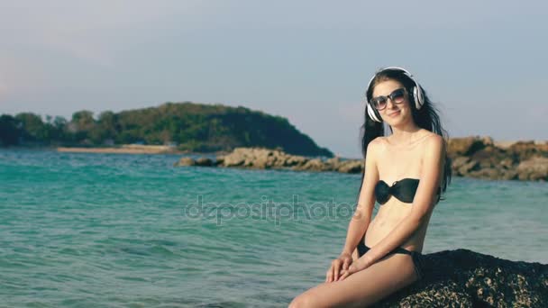 Movimento lento de mulher bonita feliz ouvindo música em fones de ouvido sem fio e dançando na praia do oceano — Vídeo de Stock