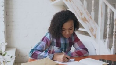 Konsantre masada oturan genç kıvırcık saçlı karışık yarış genç kız Üniversitesi sınav için öğrenme dersler odaklı
