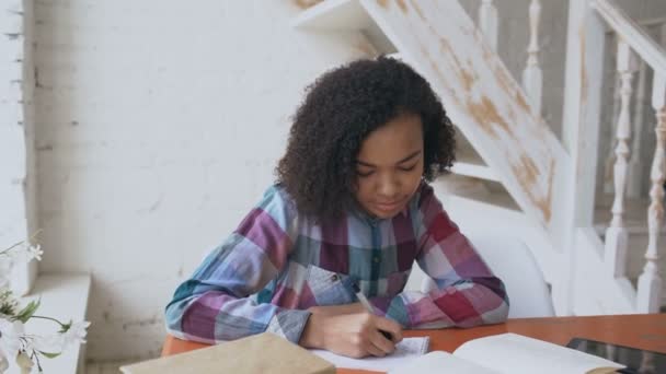 Teenage curly haired mixed race young girl sitting at the table concentrating focused learning lessons for examination to univercity — Stock Video