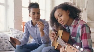 Akustik gitar evde oynamak için genç kız kardeşi öğretim yatağa oturmuş tablet bilgisayar ile karışık yarış genç kadın