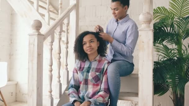 Två afrikanska amerikanska lockiga flickor sistres göra roliga krullig frisyr varandra och har roligt hemma — Stockvideo